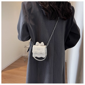 Close-up of white patent leather mini bag with bow detail and silver chain strap