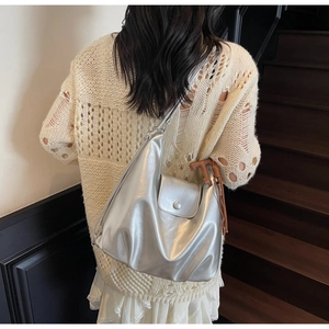 Detail of silver metallic tote bag with fold texture and brown tassel on stairs