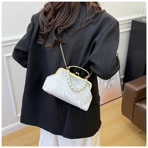 Detail of white jacquard shell bag with pearl handle and golden chain on black blazer