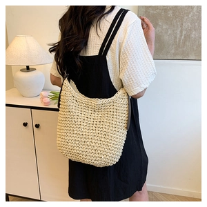 Detail of a large straw shoulder bag with dark brown leather straps and woven texture