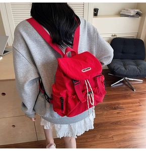 Detail of red nylon backpack showing leather logo tag and drawstring closure mechanism