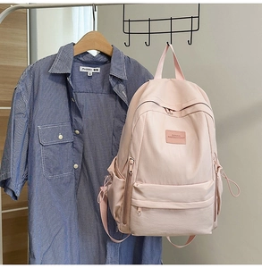 Pink nylon backpack detail showing front zipper pocket and strap on a blue plaid shirt