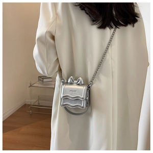 Detailed back view of a silver mini bow crossbody bag with metallic chain on white blazer
