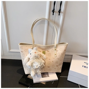 Detail of beige tote bag featuring cartoon cat prints and a plush rabbit charm accessory