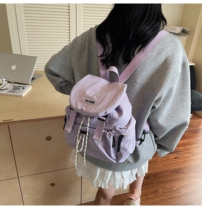 Rear view of a light purple nylon backpack worn by a model in a minimalist study setting