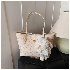 Detail of cream tote bag featuring cute cartoon bear patterns and a plush rabbit pendant