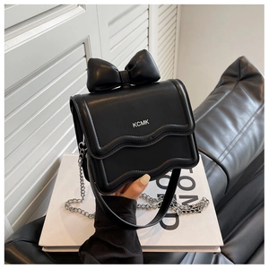 Detailed close-up of a black leather mini bag with bow accent and silver metal chain strap