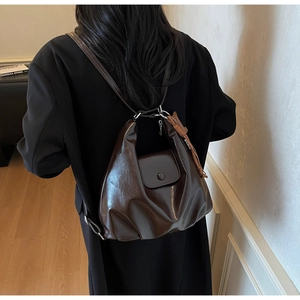 Dark brown glossy cloud tote bag shown on a model wearing a classic black coat