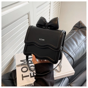 Detail of black leather crossbody bag with bow design and silver chain strap