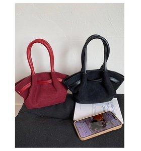 Detail view of burgundy and black suede tote bags with smooth leather handles on a sofa