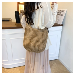 Close-up of a large khaki woven straw shoulder bag with a wide strap design