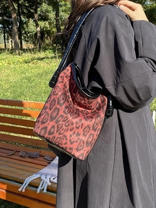 Fashionable leopard print bucket bag with black glossy straps and textured red fabric