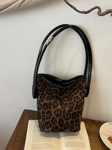 Fashionable leopard print bucket bag with black leather straps on a wooden table setup