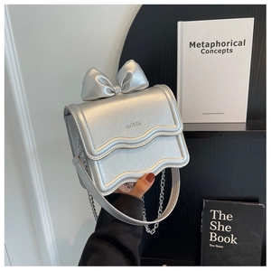 Detailed view of silver metallic bow handbag with wavy flap and KCMK brand logo