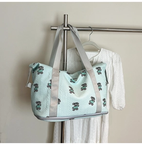Detail of mint green foldable travel bag featuring embroidered cartoon bears and gray strap