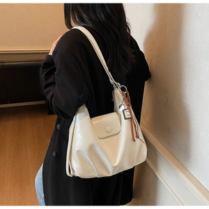 Rear view of a model wearing a cream pleated leather hobo bag with magnetic flap and charm