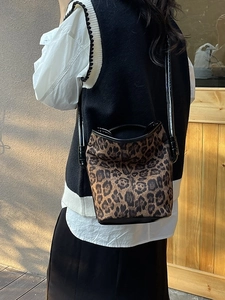 Leopard print bucket bag with black straps worn by a model in an outdoor setting