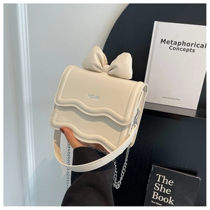 Detail of cream mini crossbody bag with a bow decoration and silver metal chain strap