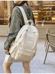 Detail of a minimalist off-white backpack featuring multiple zippers and side drawstrings