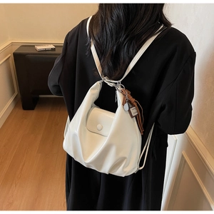 Detail of white soft leather backpack featuring elegant pleats and brown tassel charm