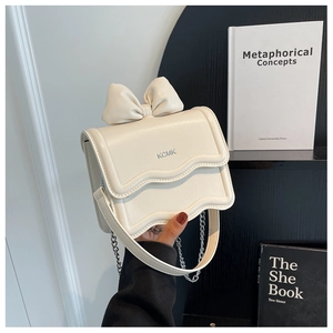 Close-up of cream bow crossbody bag with wavy flap and silver chain strap details