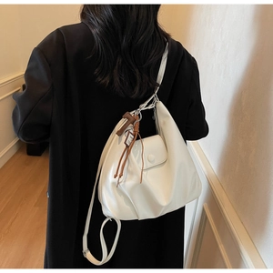 Model wearing a minimalist cream cloud shoulder bag with tassel detail and sleek PU finish