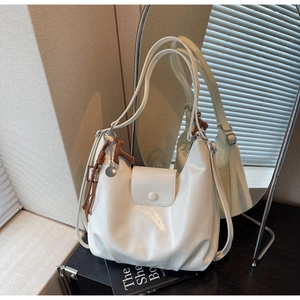 Detail of white glossy PU leather hobo bag with fringe tassel on a dark wooden surface