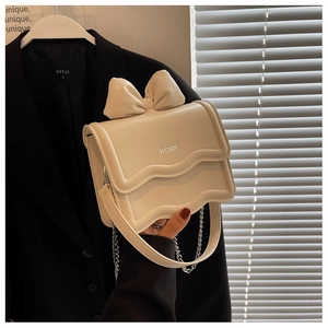 Detail of a beige bow knot mini crossbody bag with wave edges and golden chain strap