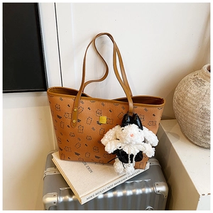 Detail of a brown tote bag with bear patterns, gold logo, and a rabbit plush charm