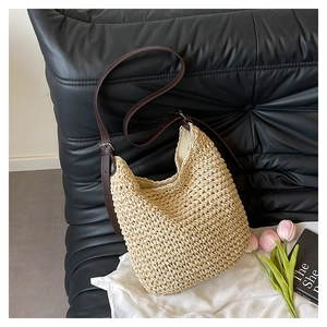 Detail of handwoven straw bag with dark brown leather strap on a textured black sofa