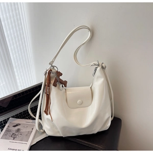 Detail of white moon-shaped hobo bag with H-charm and tassel on a stylish desk setup
