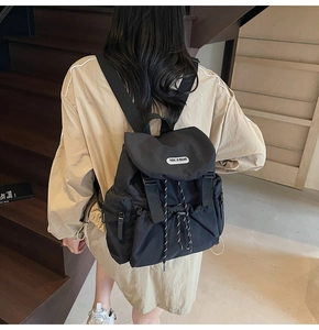 On-body view of a stylish black nylon backpack with flap cover and drawstring closure