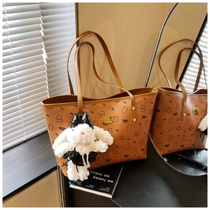 Detail of a brown tote bag with bear print, gold hardware, and a plush bunny charm accessory