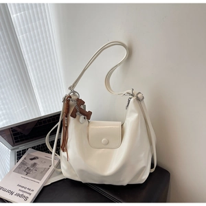 Detail of off-white hobo bag with glossy finish, flap closure and leather tassel charm