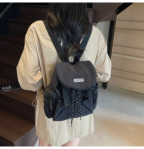 Detail of black nylon backpack featuring drawstring closure and side zipper pocket