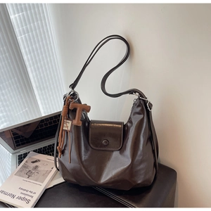 Detail of dark brown glossy leather shoulder bag with T-letter tassel charm and soft texture