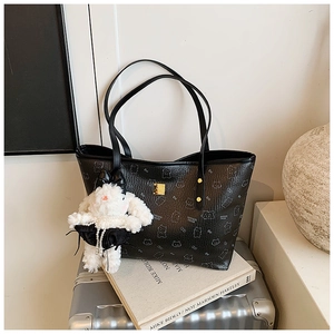 Black leather tote bag with cat patterns and white bunny pendant on a metal suitcase