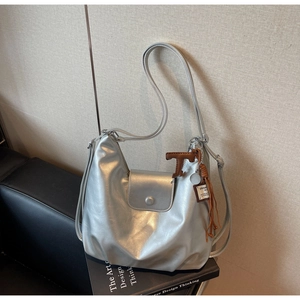 Détail du sac argenté mat avec fermoir magnétique, pompon et pendentif lettre