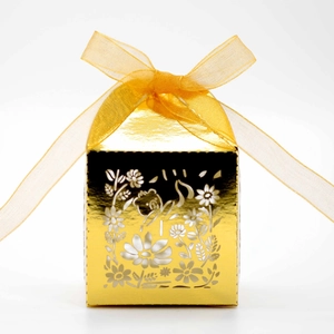 Detail of laser-cut golden favor box featuring intricate floral patterns and yellow silk ribbon