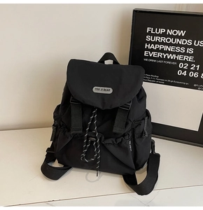 Detail of black nylon backpack with flap buckle closure and grey YOU JI BEAR logo patch