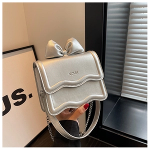 Close-up of a silver bow mini bag with KCMK logo, chain strap, and metallic finish