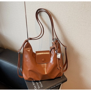Détail d'un sac à épaule en cuir marron caramel sur un livre avec un pendentif en métal