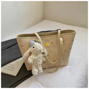 Detail of a large cream tote bag with bear print and a plush rabbit charm on a bed