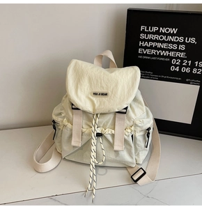Detail of cream nylon backpack with textured fabric, drawstring flap, and woven brand tag