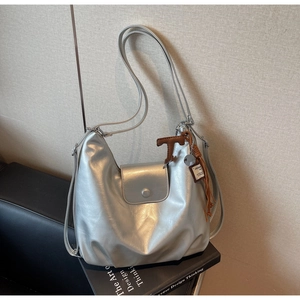 Detail of silver metallic hobo bag featuring a brown letter T charm and leather tassel