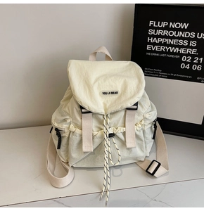 Detail showing cream nylon backpack with flap closure, dual buckles, and drawstring cord