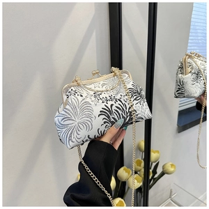 Detailed close-up of white fabric shell bag with elegant black floral embroidery and gold clasp