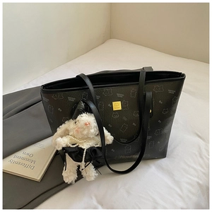 Detail of black tote bag with bear print and cute plush rabbit charm on a bed