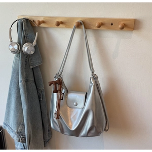 Detail of silver metallic hobo bag with 'T' charm and tassel on wooden hook hanger