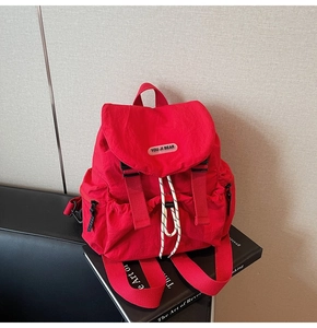 Detail of red nylon backpack with flap closure, drawstring, and You Ji Bear logo